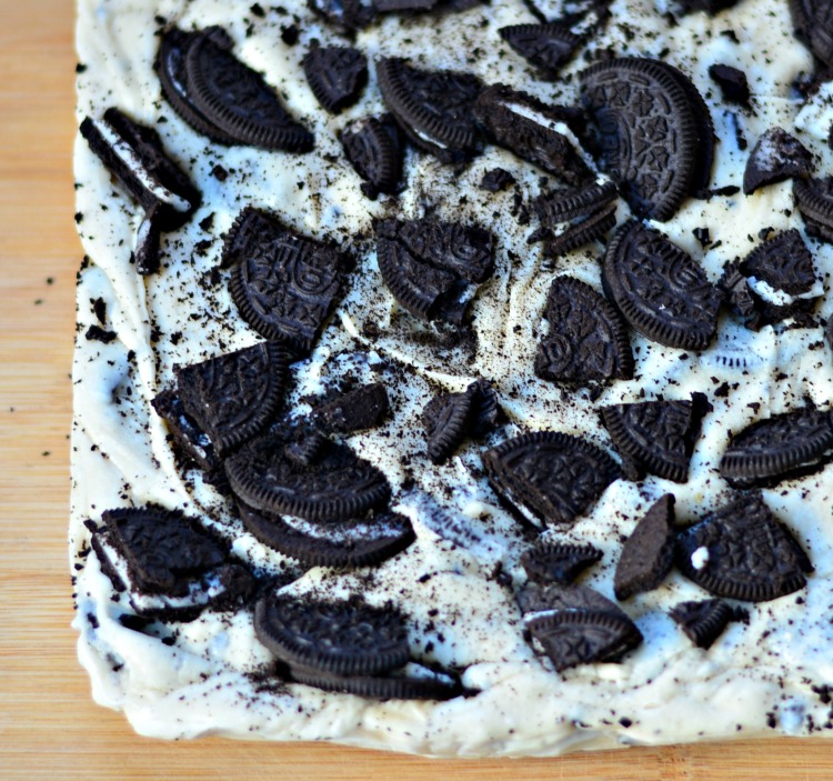 A slab of homemade cookies and cream fudge laying on a wooden counter ready to be cut