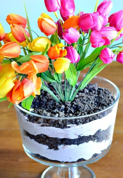 Discover how to make a dirt cake that is both yummy and elegant! This chocolate dirt cake is served in an elegant footed serving dish and topped with bright spring flowers for a centerpiece that is both gorgeous and delicious!