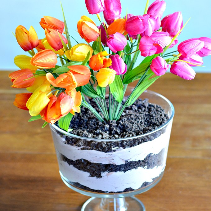 Discover how to make a dirt cake that is both yummy and elegant! This chocolate dirt cake is served in an elegant footed serving dish and topped with bright spring flowers for a centerpiece that is both gorgeous and delicious!