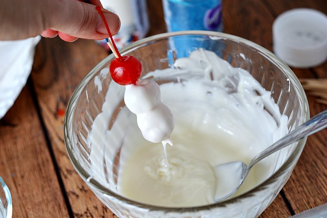 Dipping maraschino cherries on a toothpick in to melted white chocolate