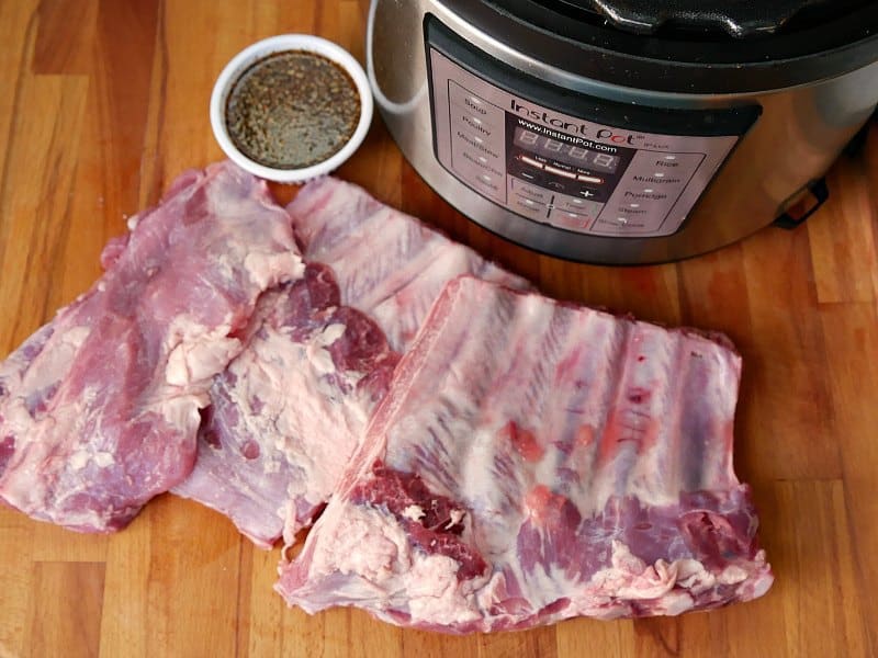A rack of raw pork spare ribs cut in to three equal pieces as they are prepared to be seasoned and then cooked in the Instant Pot.