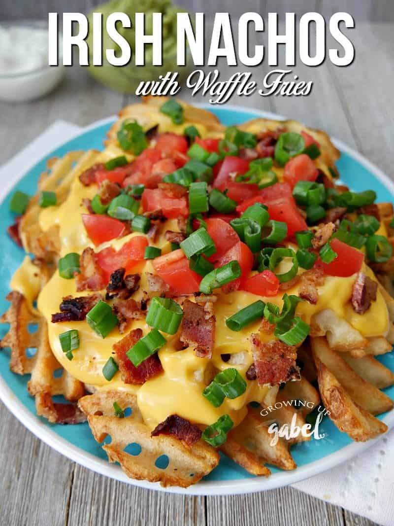 A plate full of finished Irish Nachos Recipe made with waffle fries, bacon, tomatoes, onions and nacho cheese sauce. 