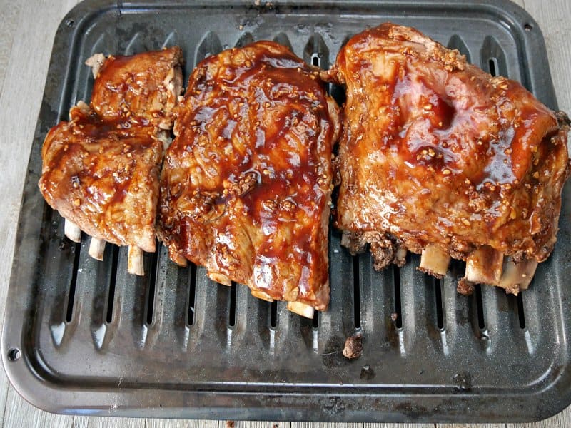 Three pieces of spare ribs cooked and covered in barbecue sauce on a broiler pan for browning. 