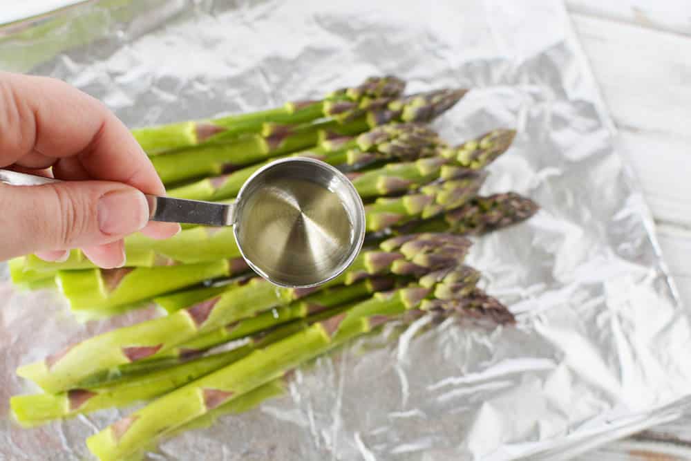 A tablespoon of oil with asparagus in the background.
