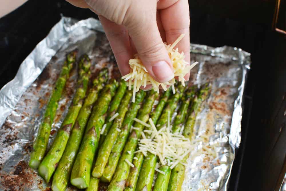 Grilled asparagus on grill being covered in cheese