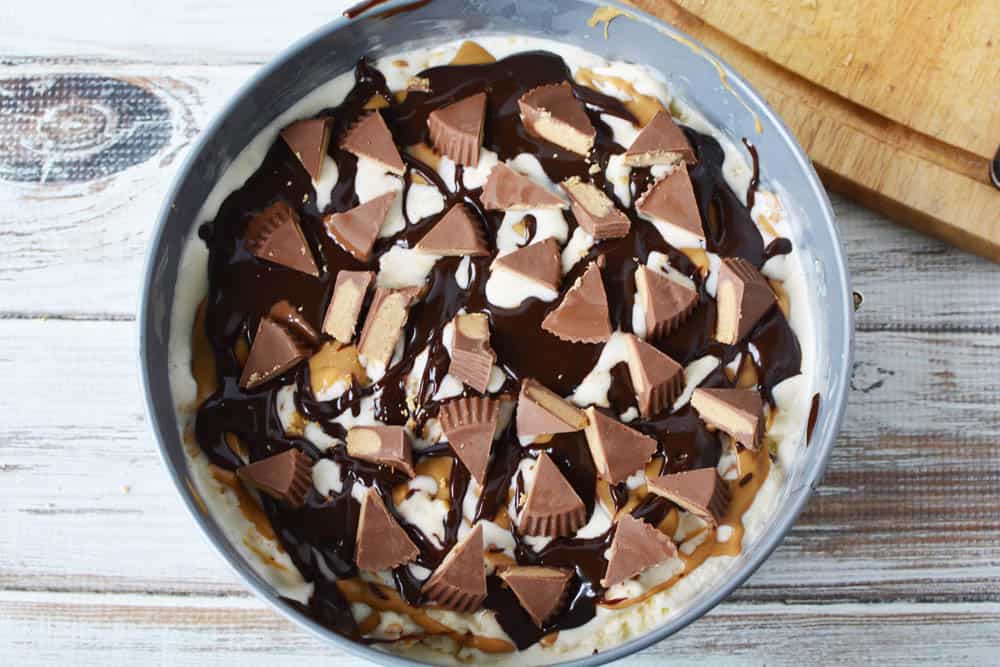Ice cream in cake pan topped with peanut butter, hot fudge and chopped peanut butter cup candy