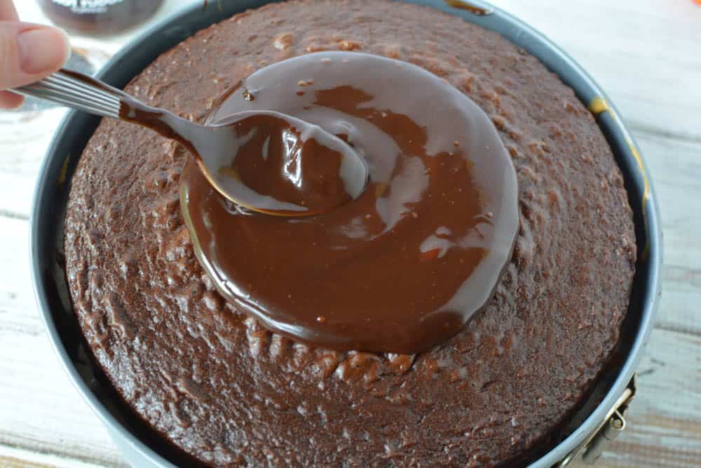 Round chocolate cake topped with melted hot fudge being spread by a spoon