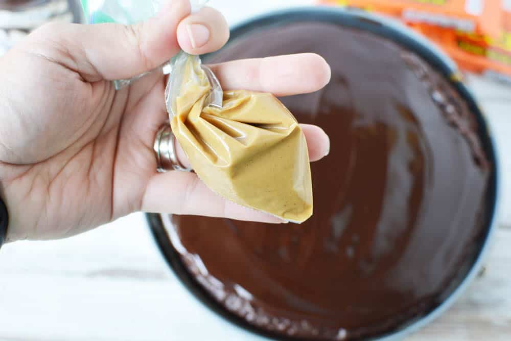 Melted peanut butter in a plastic storage bag above a chocolate cake topped with hot fudge