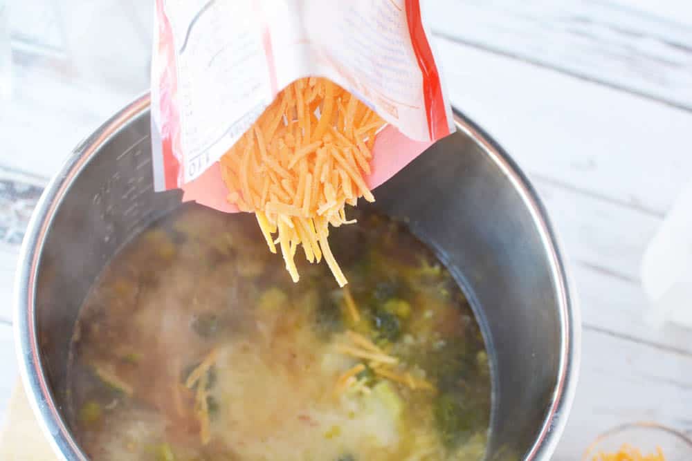 Shredded cheese being dumped into an Instant Pot broccoli cheese soup recipe