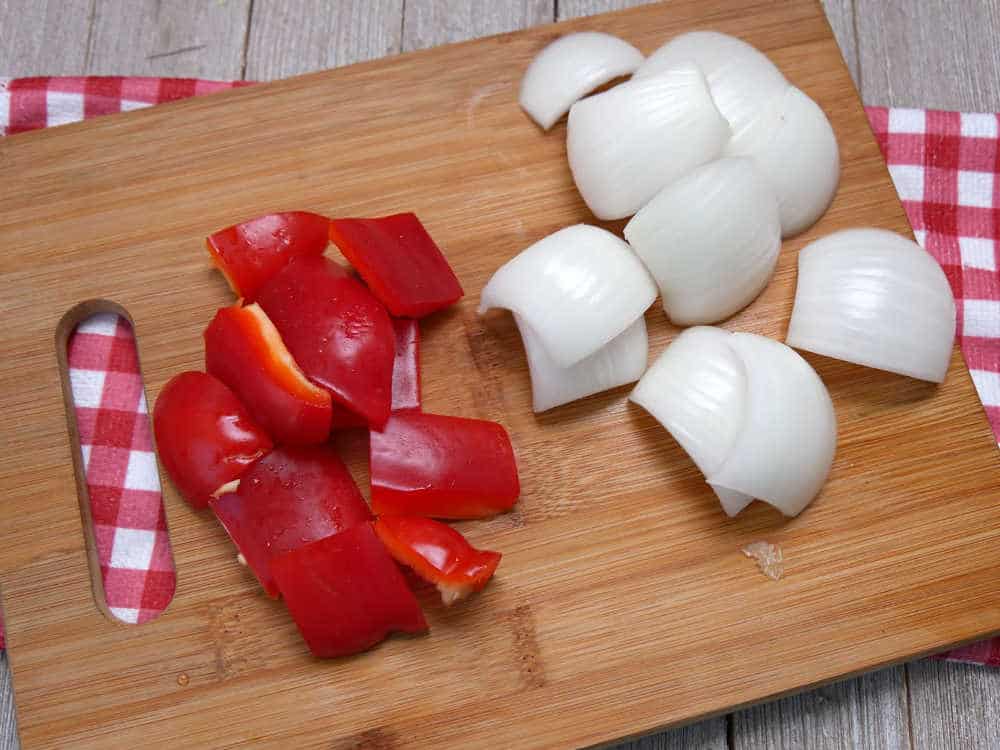 Red bell pepper and white onion cut up in to large chunks on a cutting board
