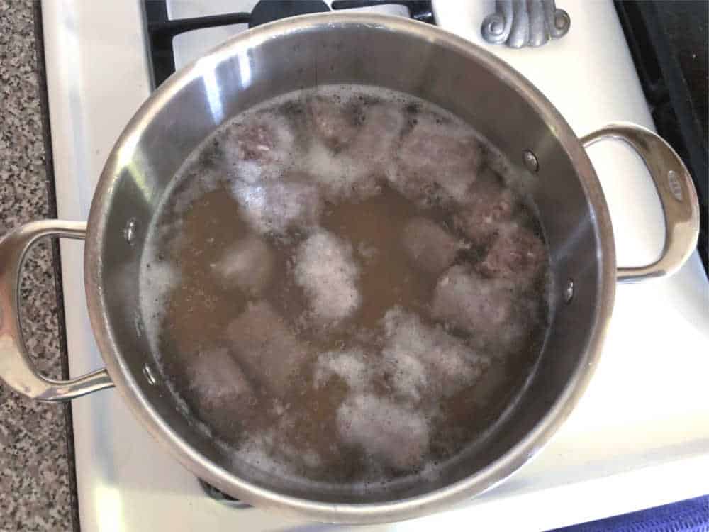 Pieces of brats boiling in liquid in a pot on a stove