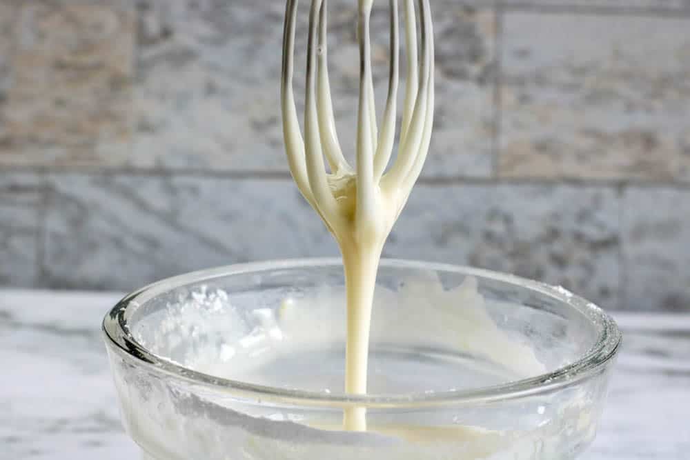 Glaze frosting dripping off a whisk into a bowl