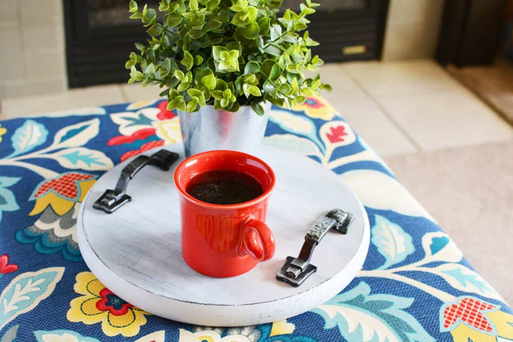 wood tray on floral ottoman with a red cup of coffee and plant on it