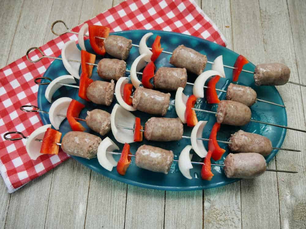 brats, onions, and red peppers on kebab skewers on a platter