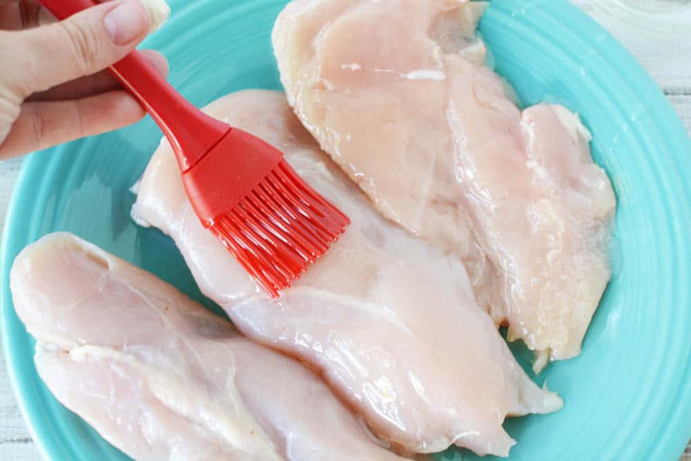 Red pastry brush coating chicken breasts in oil 