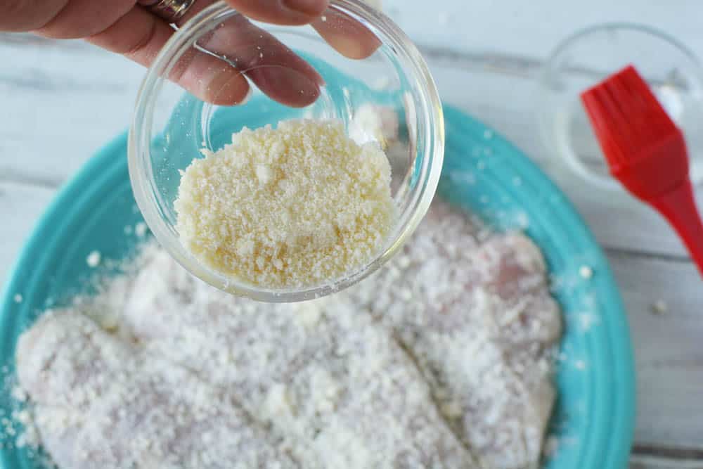 A bowl of grated Parmesan cheese being put on chicken breasts