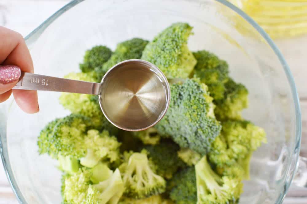 tablespoon of oil over a bowl of fresh broccoli