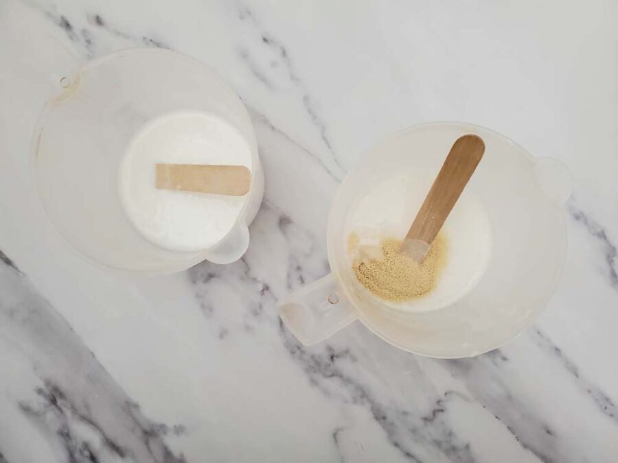 Melted soap base in measuring cups with wooden sticks for stirring and one with powdered honey