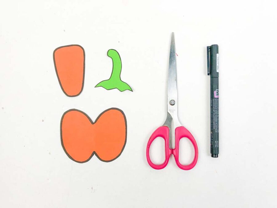 Orange pumpkin pieces, green stem, scissors, black marker
