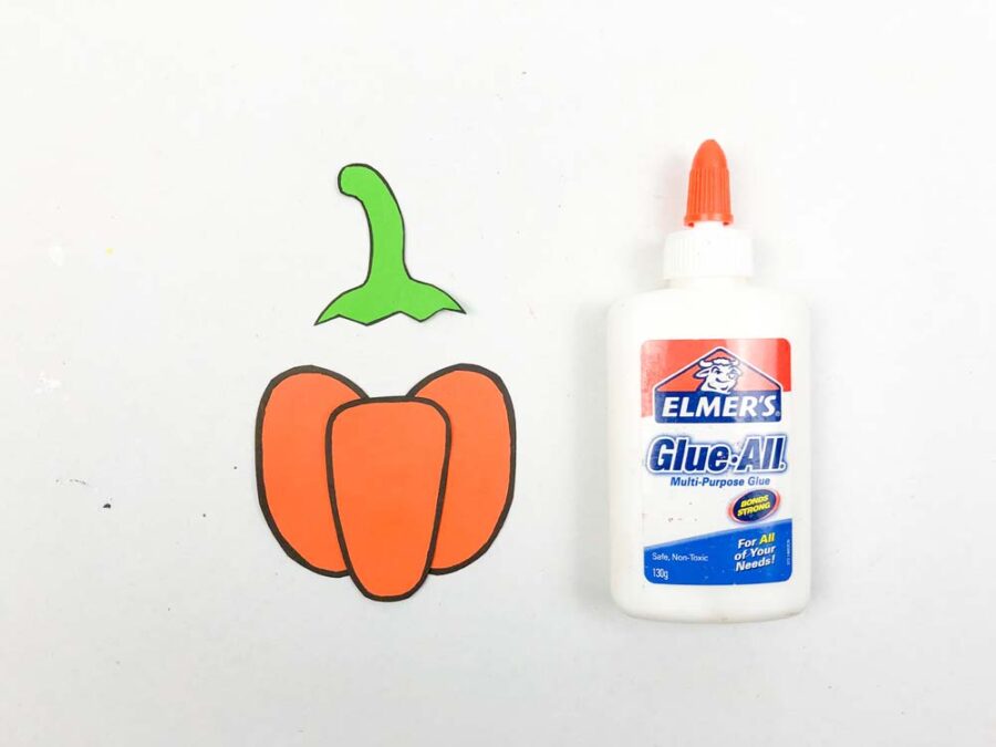 Orange pumpkin pieces, green pumpkin stem, a bottle of glue