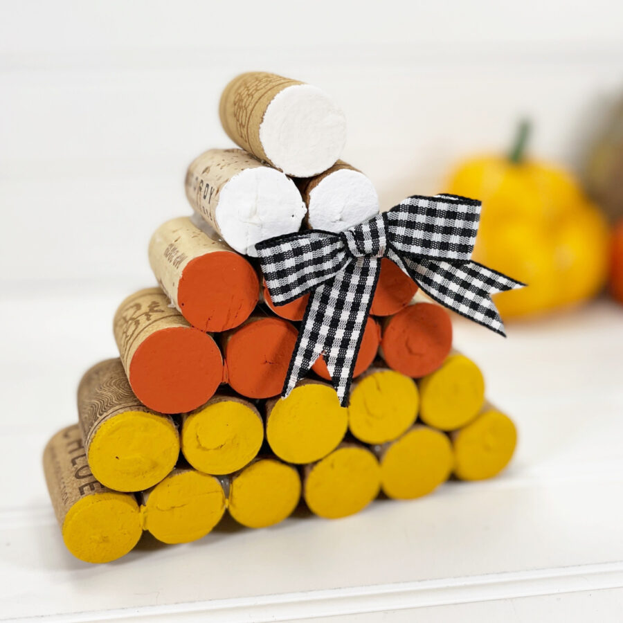 Wine Corks stacked in the shape of a candy corn with the colors white on the top orange in the middle and yellow on the bottom with a plaid black and white bow