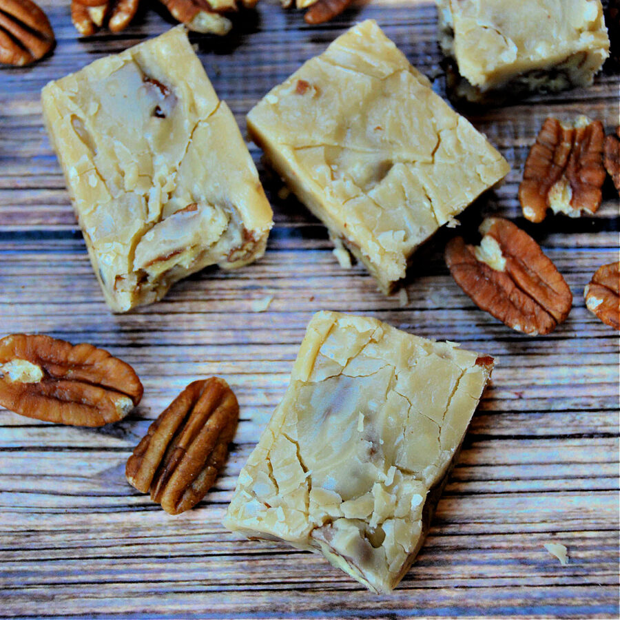 Pieces of butter pecan fudge on a table with pecans