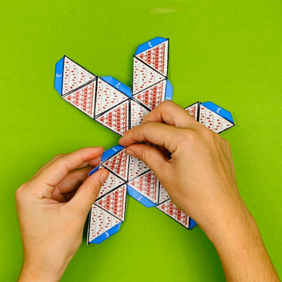 A person folding down tabs of a print and fold paper Christmas tree ornament craft