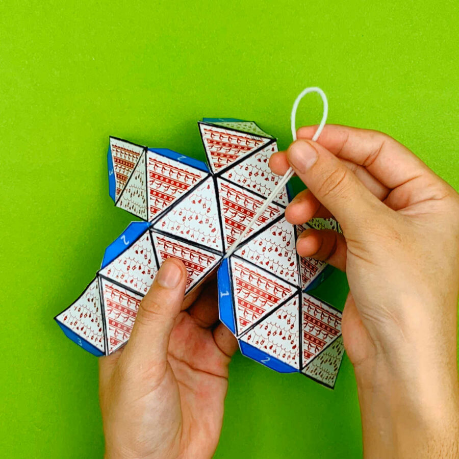 A person adding a string hanger to the center of a print and fold paper Christmas tree ornament craft