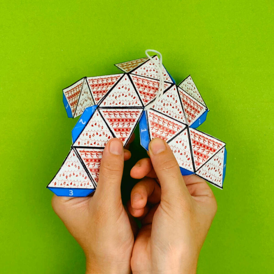 A person folding down tabs 1 of a print and fold paper Christmas tree ornament craft
