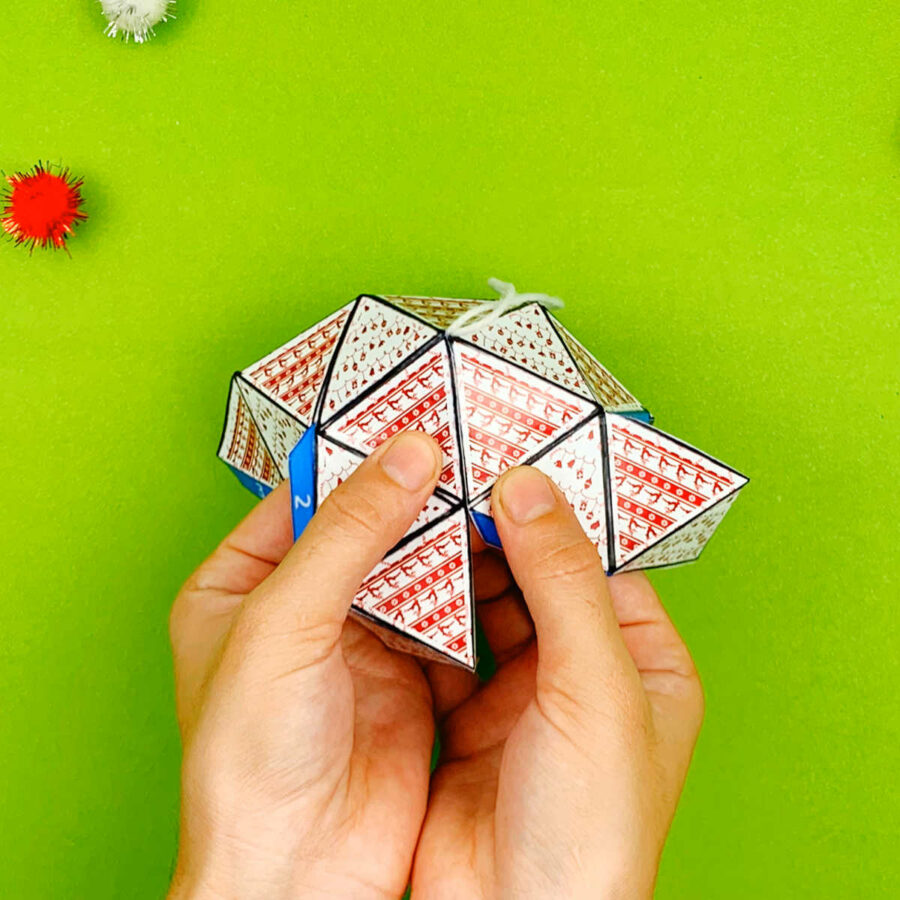 A person holding together some tabs of a print and fold paper Christmas tree ornament craft