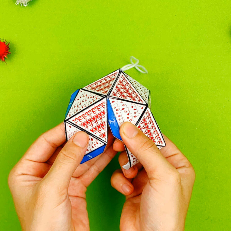A person gluing tabs 2 of a print and fold paper Christmas tree ornament craft