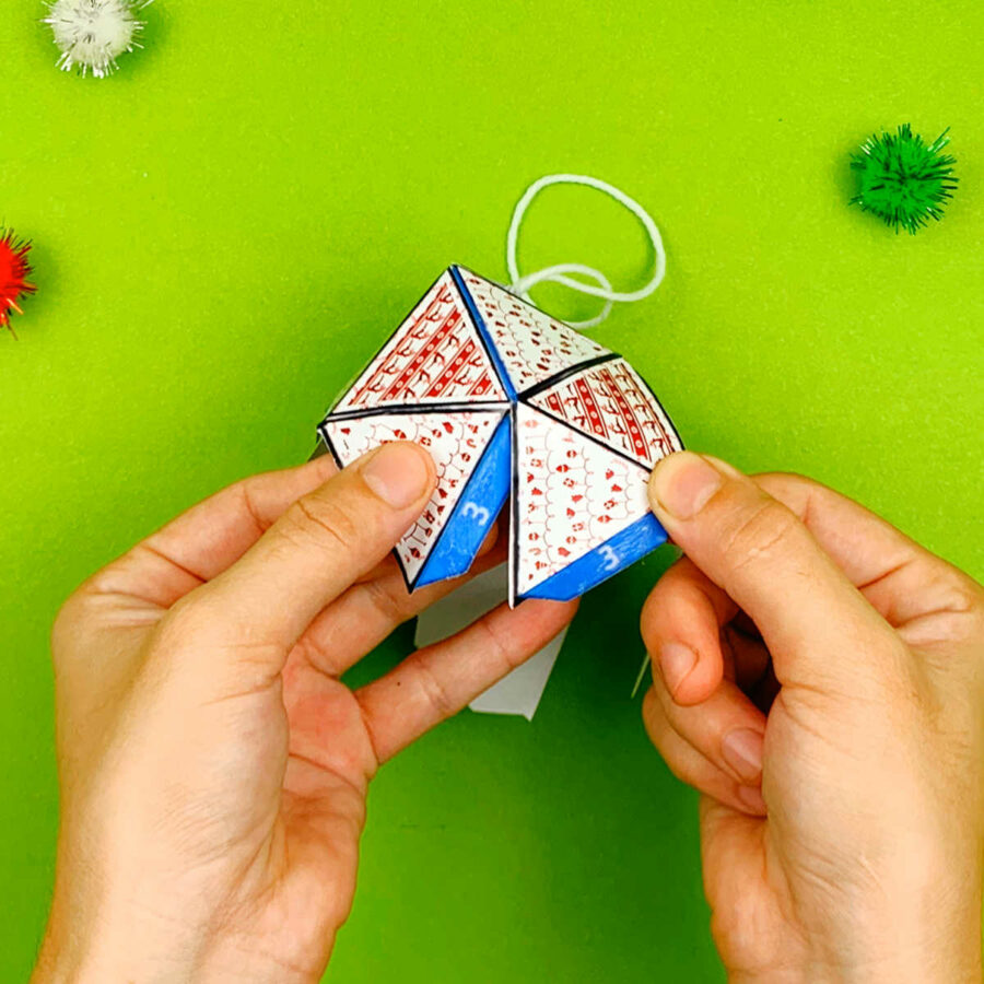 A person gluing down tabs 3of a print and fold paper Christmas tree ornament craft